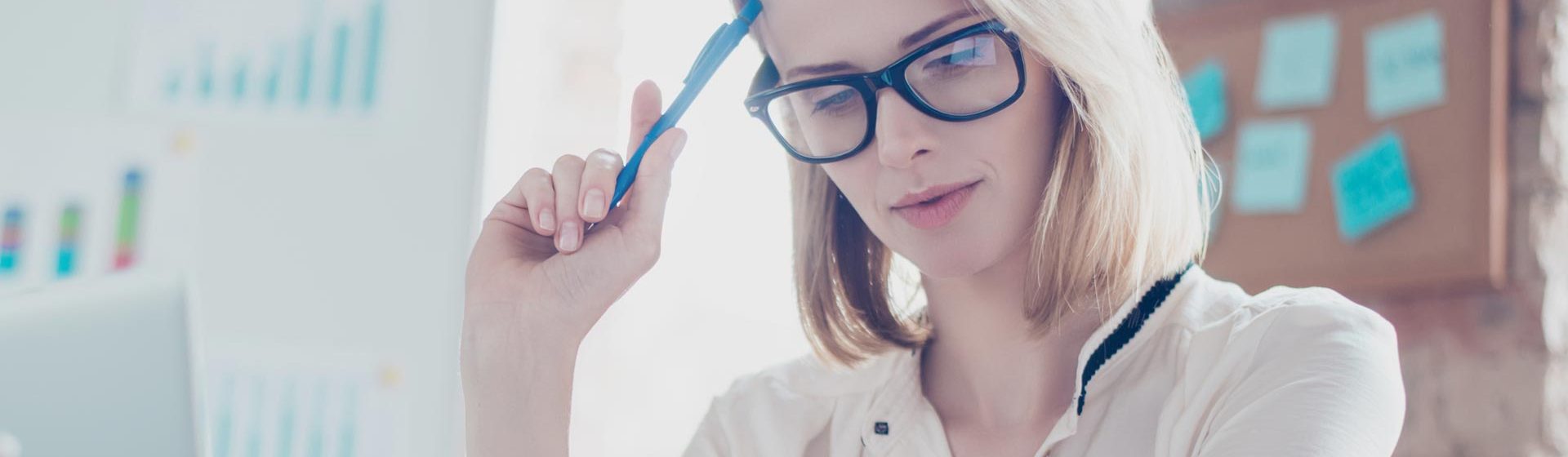 HR professional thinking about her retention strategy while reviewing HR data and analytics with glasses on and a pen in her office