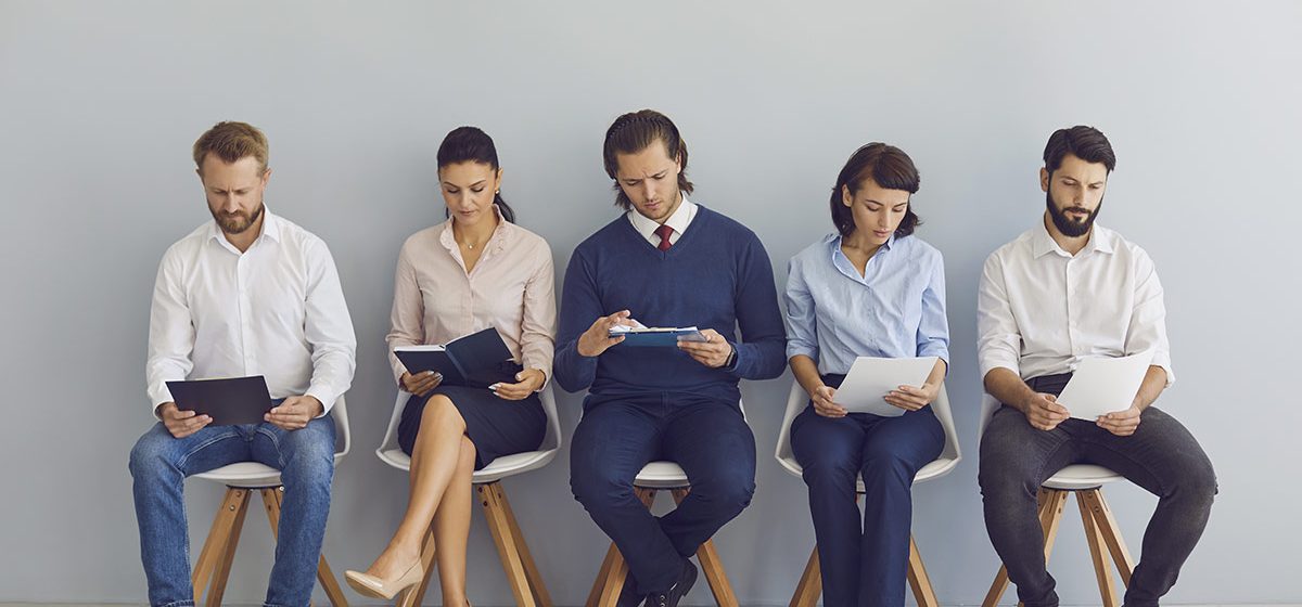 Job seekers with resumes in hands waiting for job interview sitting on chairs in a row