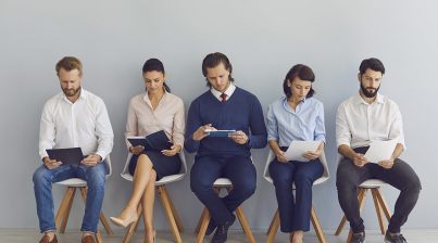 Job seekers with resumes in hands waiting for job interview sitting on chairs in a row