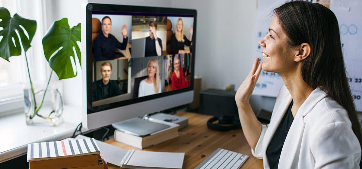 Remote worker waves to team on virtual video conference at her desk in her home office