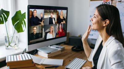 Remote worker waves to team on virtual video conference at her desk in her home office