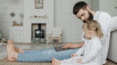 Father working on laptop next to child