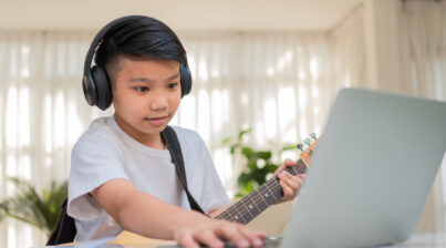 Boy playing guitar while looking at a laptop