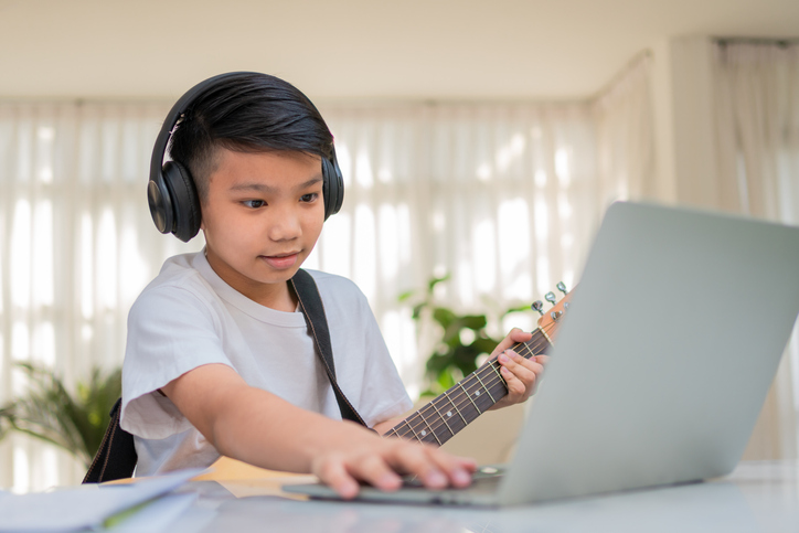 Boy playing guitar while looking at a laptop