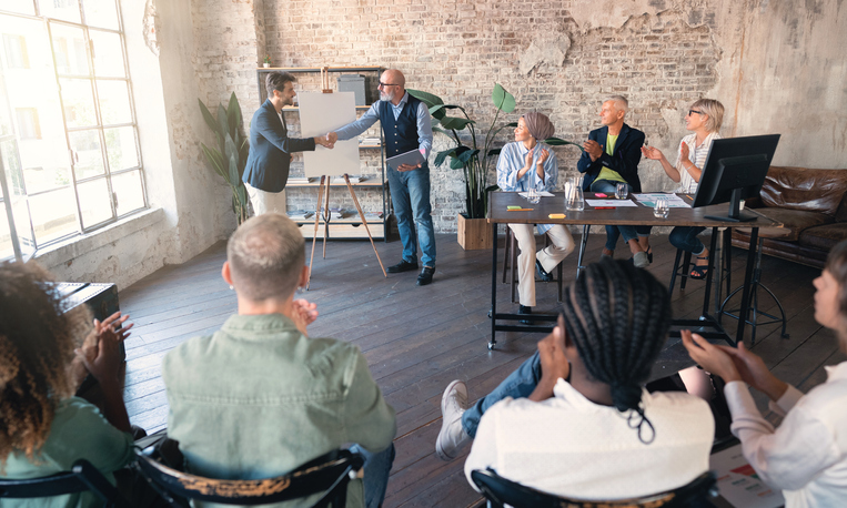 Two businessman shaking hands in front of a group of people in the office