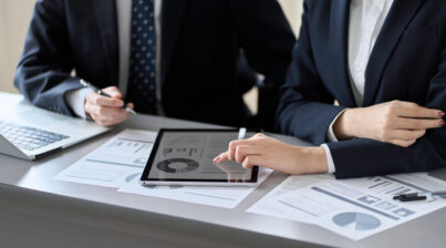 Two people looking at data on a tablet and on paper reports