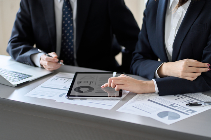 Two people looking at data on a tablet and on paper reports