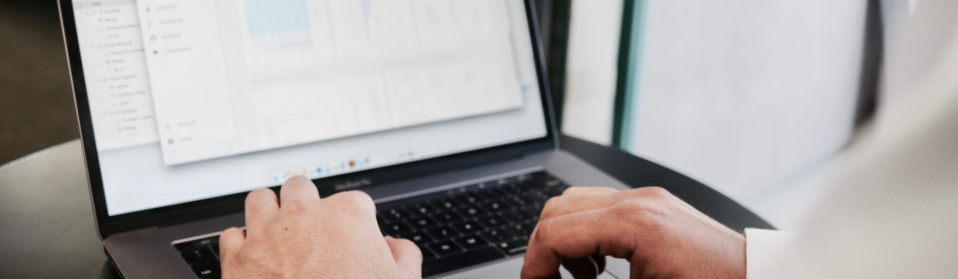 Man's hands typing on a laptop with screen showing data and graphs