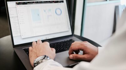 Man's hands typing on a laptop with screen showing data and graphs